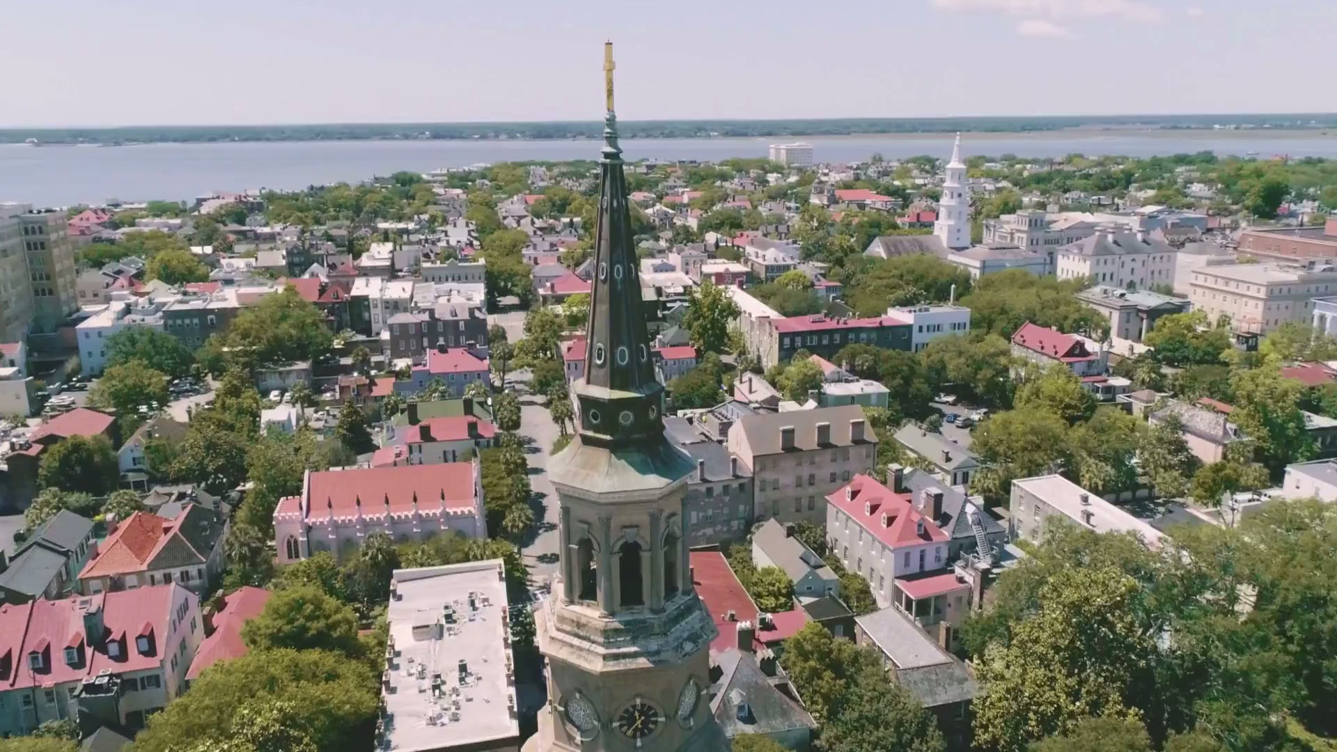 Aerial orbit around the spire of St. Philip's Church over Charleston's historic district with the harbor beyond